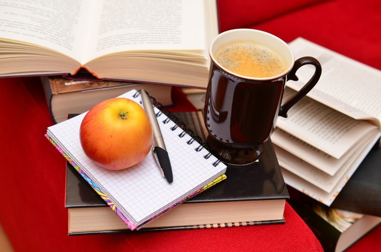 Bild på böcker, kaffe, skrivmaterial och äpple. Allt man behöver för att göra en bra översättning.