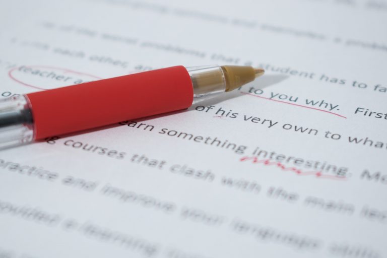 En röd penna som ligger på ett papper med text. Texten har röda markeringar.
